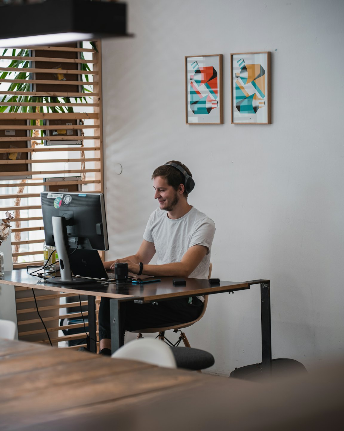 Man with headphones smiles while working on computers at a desk.