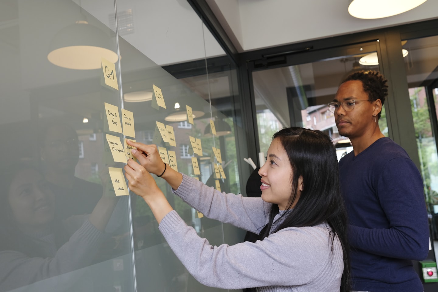 Two professionals collaborating on tasks on a glass partition.